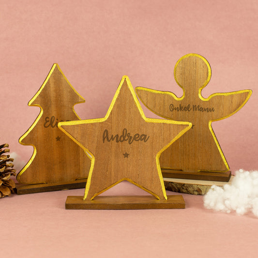 Mehrere weihnachtliche Holzfiguren in unterschiedlichen Größen – Sterne, Engel und Tannenbäume mit goldfarbenem Rand, auf Holzsockeln stehend, dekorativ arrangiert vor hellem Hintergrund.