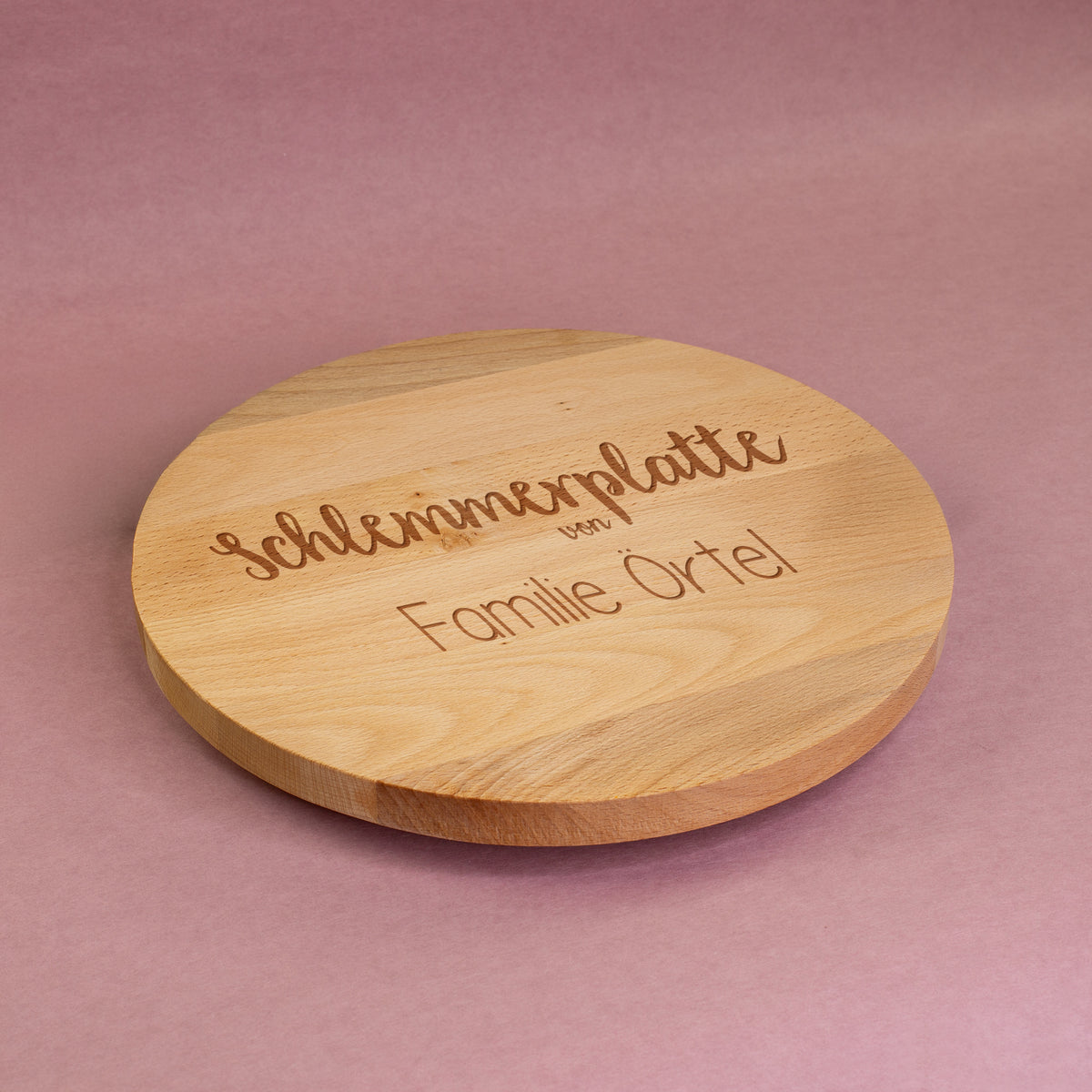 Drehbare Servierplatte aus Buchenholz mit Gravur „Schlemmerplatte von Familie Örtel“, dekorativ auf rosa Untergrund