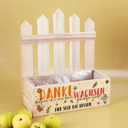 Leere Pflanzkiste mit Zaun, bedruckt mit „Danke, dass ihr uns beim Wachsen geholfen habt“ und Wunschtext „Ihr seid die Besten“