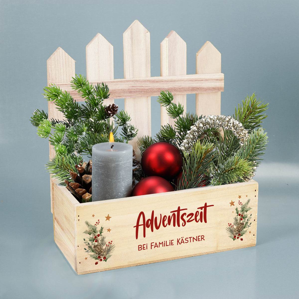 Winterliche Pflanzkiste mit Zaun, Tannenzweigen, Zapfen und roten Kugeln als Adventsdekoration