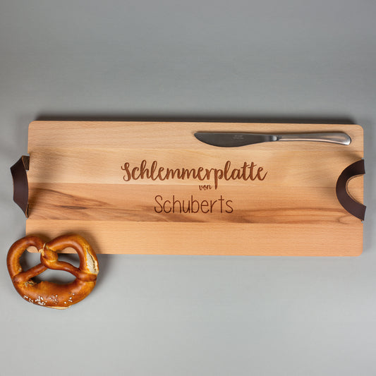 Servierbrett „Schlemmerplatte von Schuberts“ aus Buchenholz mit Ledergriffen, frontal fotografiert mit Brezel und Messer.