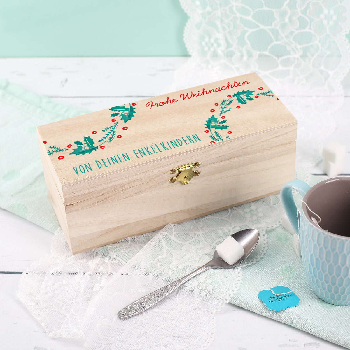 Weihnachtliche Holz-Teebox mit Mistelzweig-Verzierung und individueller Aufschrift, dekoriert neben Teetasse und Zuckerwürfeln