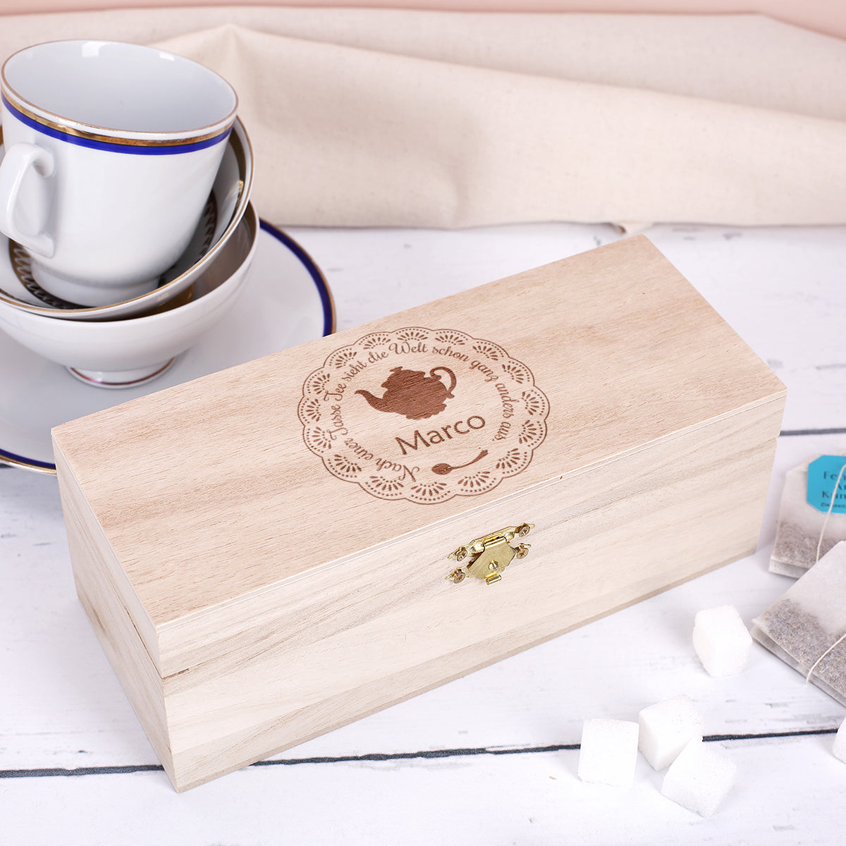 Personalisierte Teebox aus Holz mit Gravur und Name Marco, daneben Teetassen, Teebeutel und Zuckerstückchen.
