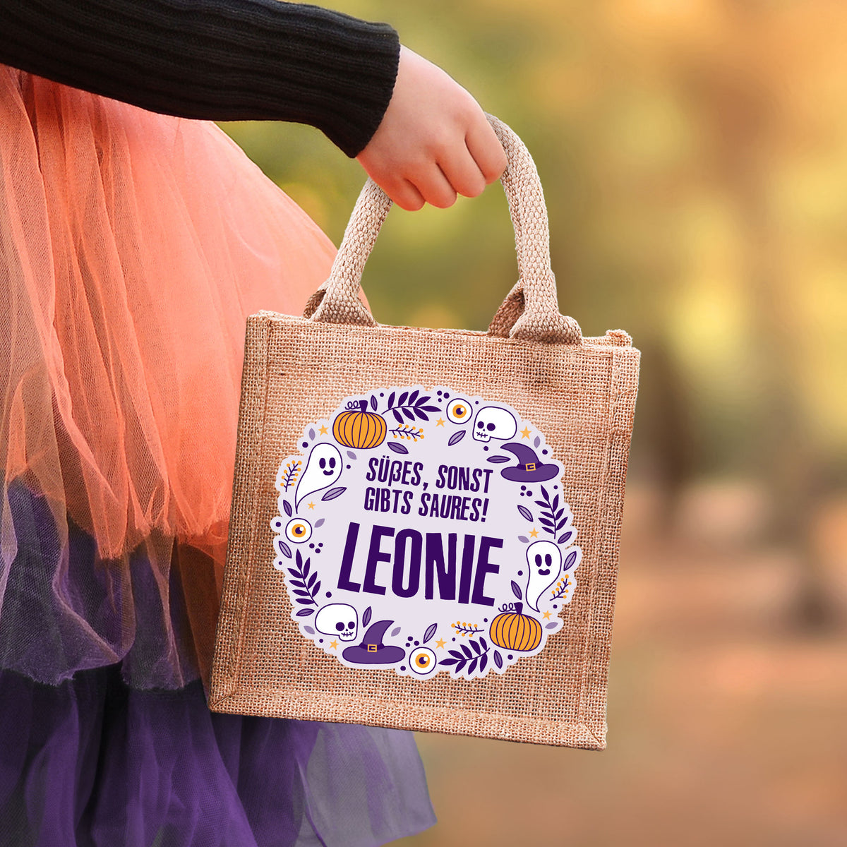 Halloween-Jutetasche mit Aufdruck „Süßes, sonst gibt’s Saures!“ und personalisiertem Namen, getragen von einem Kind im Halloweenkostüm.