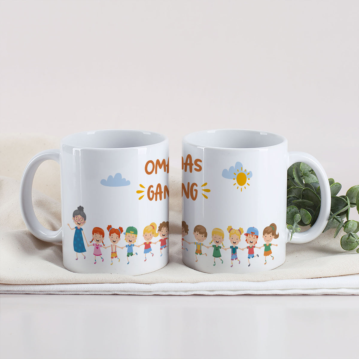 Zwei Tasse mit Motiv „Omas Gang“, Oma und eine Gruppe Kinderfiguren, auf einem weißen Tuch mit Eukalyptuszweig.