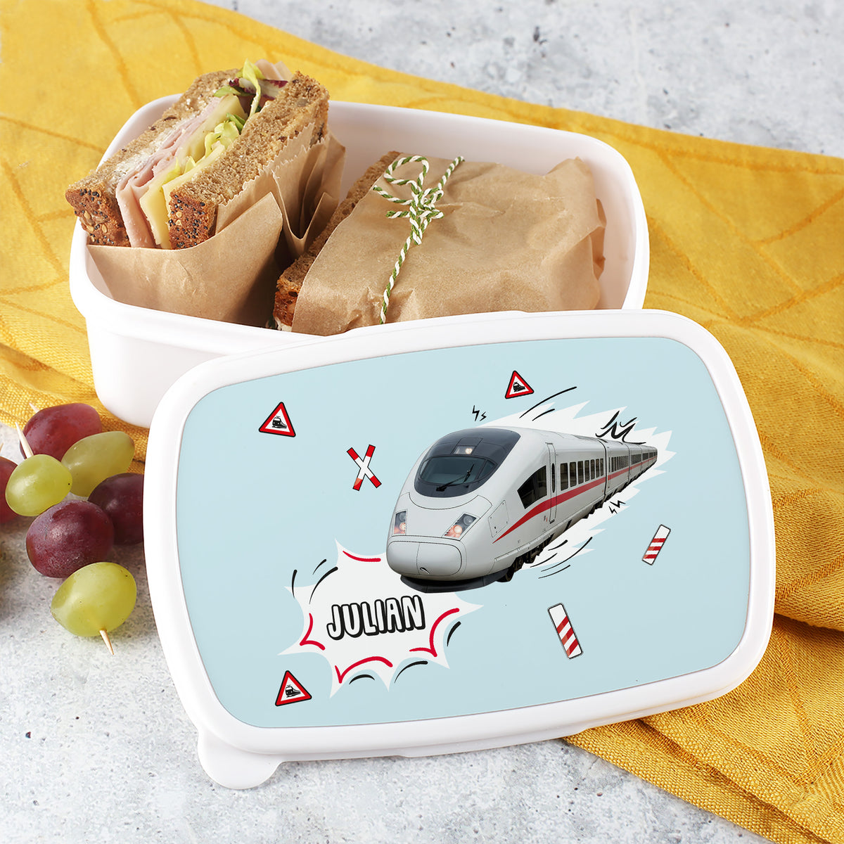 Brotdose ICE Motiv – geöffnet mit belegten Broten und Trauben auf gelben Tuch