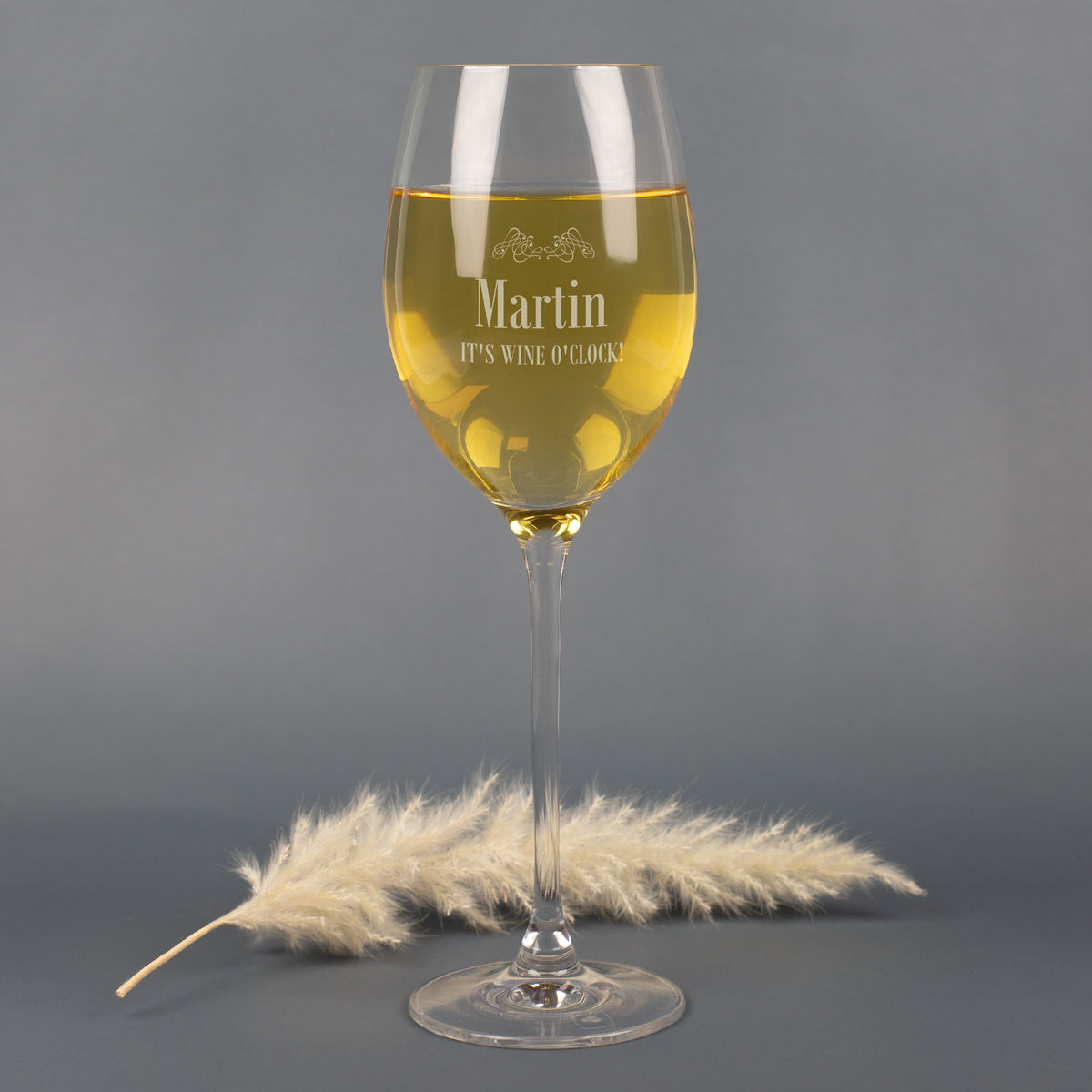 Personalisierbares Leonardo Weißweinglas mit Gravur Martin und Spruch It’s Wine O’Clock, auf grauem Hintergrund mit Pampasgras