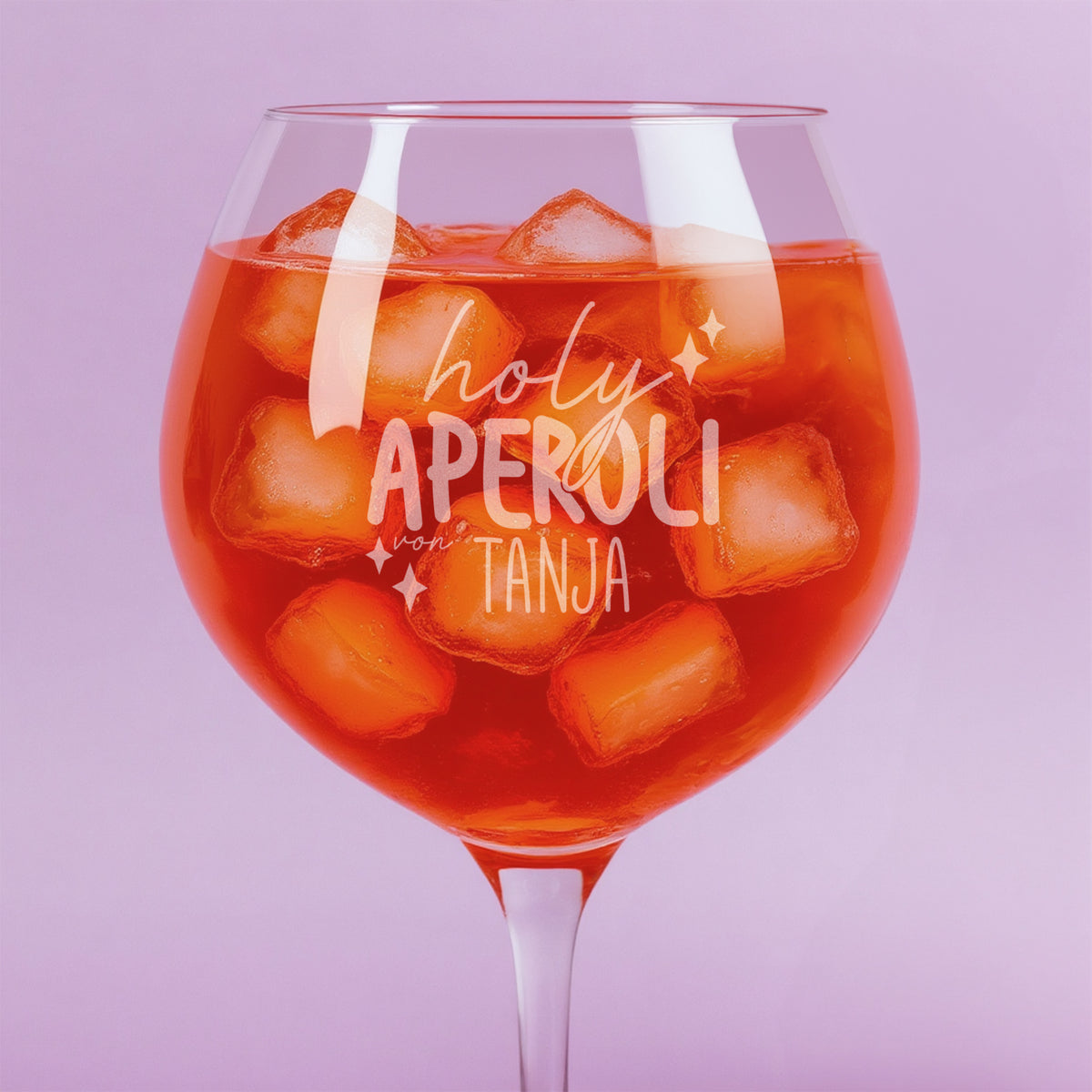 Nahaufnahme der Gravur „holy aperoli von Tanja“ auf gefülltem Weinglas mit Eiswürfeln – feine Lasergravur mit verspieltem Schriftzug und Sternmotiven.