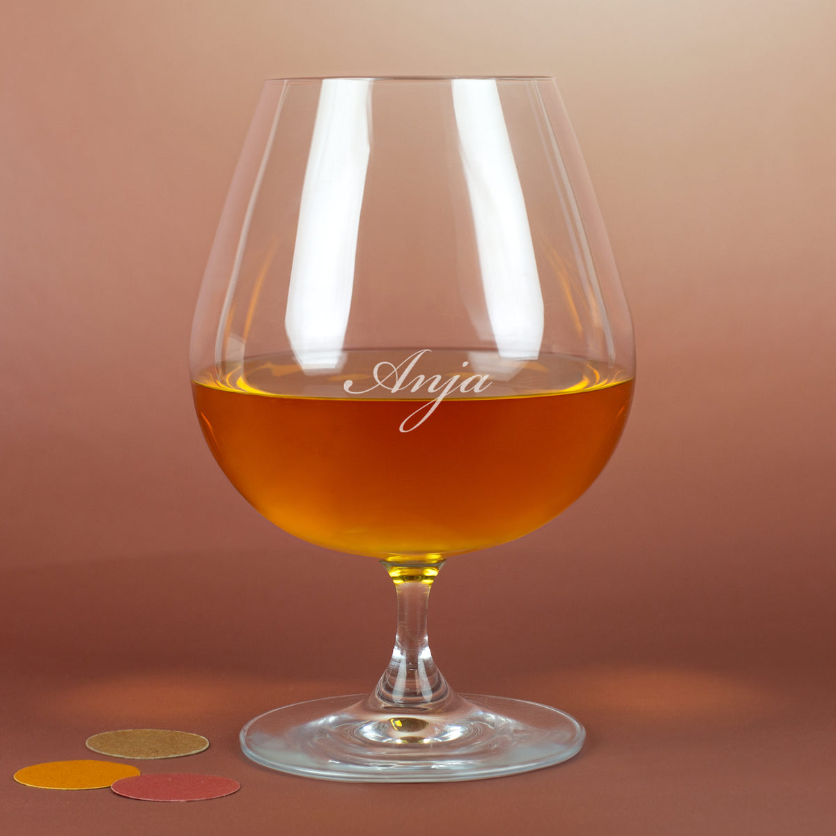 Personalisierter Cognacschwenker mit Gravur „Anja“ – edles Glas auf rötlichem Hintergrund mit Deko-Elementen.