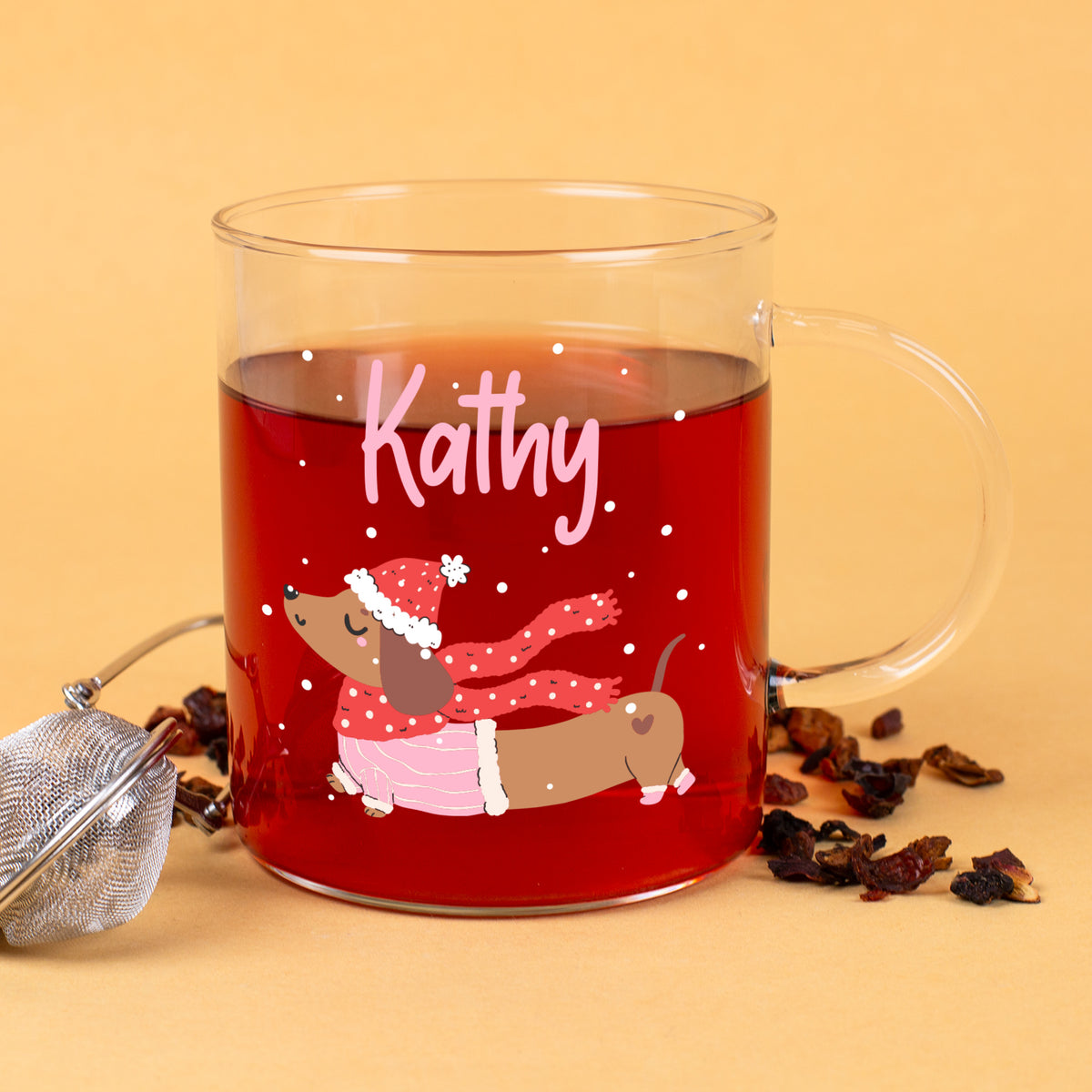 Personalisierte Glastasse mit Dackelmotiv und Name „Kathy“, aufgelöster Tee und Teesieb daneben