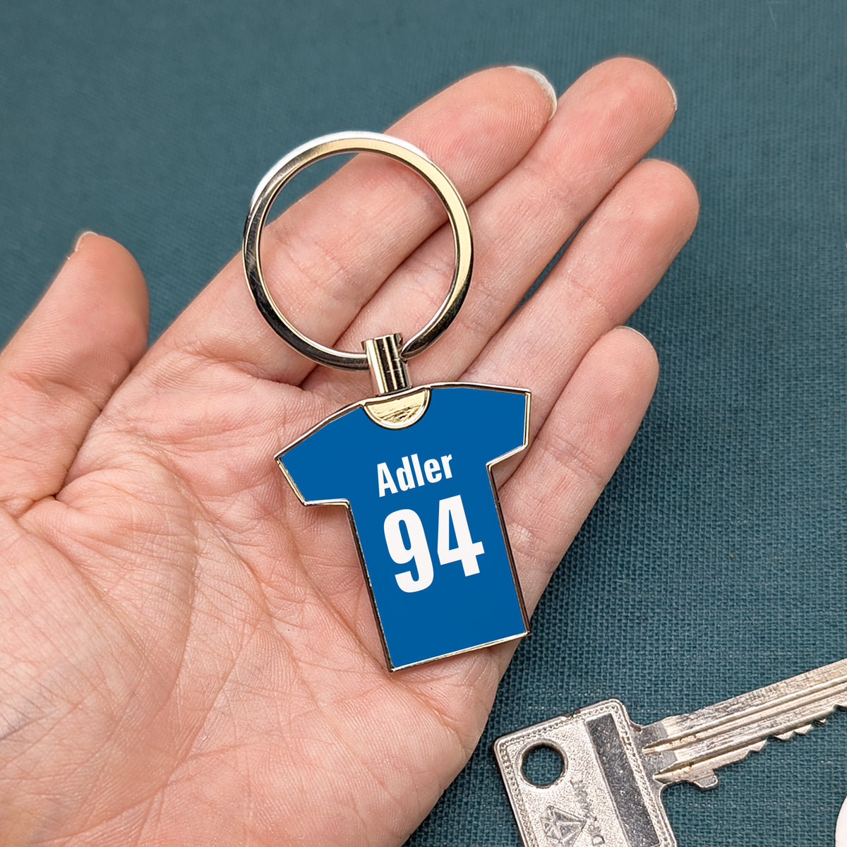 Blauer Trikot-Schlüsselanhänger mit „Adler 94“ in Hand gehalten