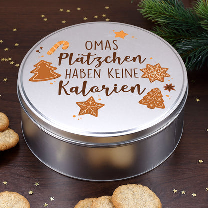 Runde silberne Blechdose mit Weihnachtsmotiv und Spruch „Plätzchen haben keine Kalorien“, dekoriert mit Tannenzweigen und Weihnachtsgebäck.