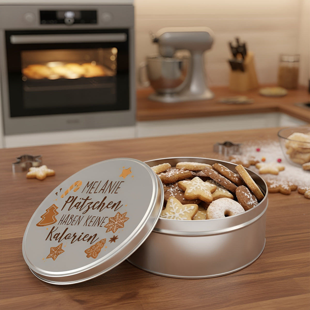 Runde Blechdose mit Spruch „Plätzchen haben keine Kalorien“ und Name Melanie, gefüllt mit Weihnachtsplätzchen in einer Küche mit Backofen im Hintergrund.