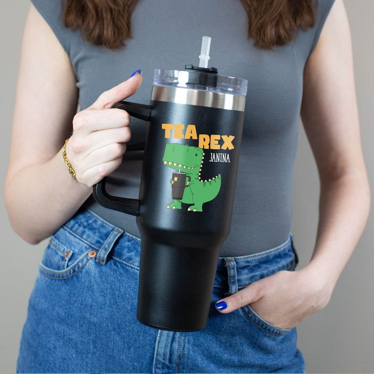 Person hält Thermobecher mit grünem Dino und „Tea Rex“-Schriftzug mit einer Hand