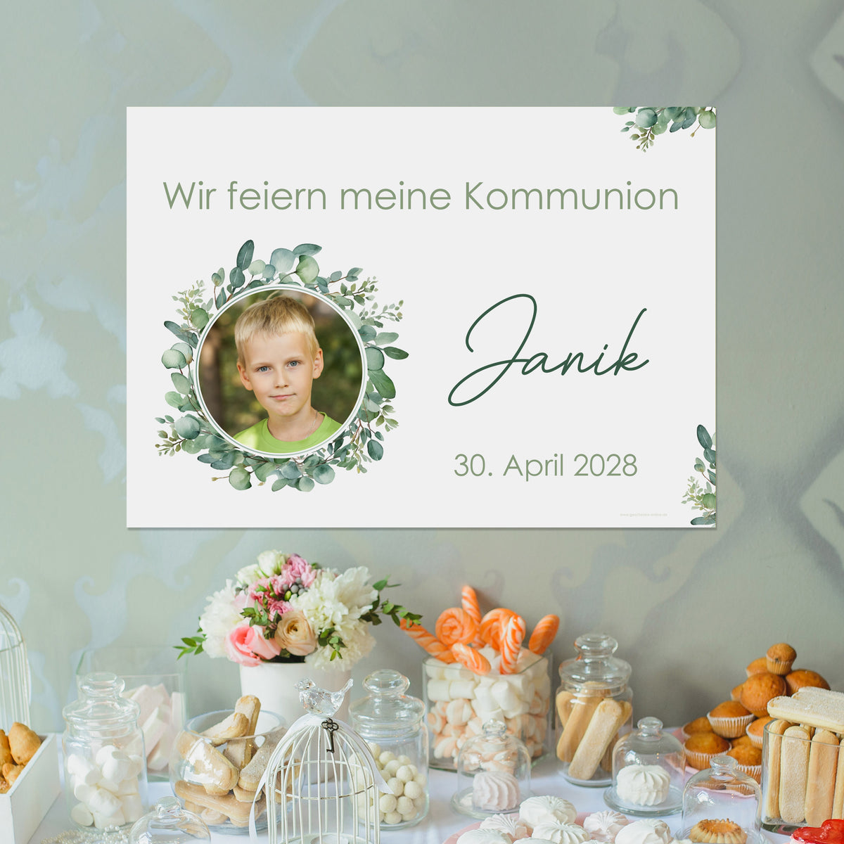 Personalisierbares Banner mit Eukalyptuskranz und Foto eines Jungen, dekorativ aufgehängt über einem Sweet Table. Text: „Wir feiern meine Kommunion – Janik – 30. April 2028“. Bannerdesign in Grüntönen mit elegantem Schriftzug.