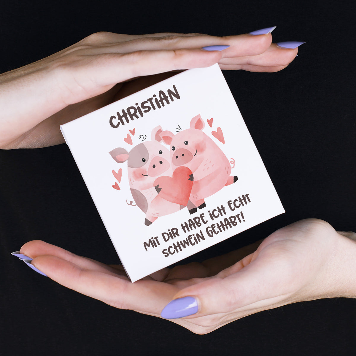 Nahaufnahme des Motivs auf dem Einleger: Zwei niedliche Schweine mit rosa und grauen Flecken sitzen nebeneinander, umgeben von Herzsymbolen. In ihren Hufen halten sie ein großes rotes Herz.