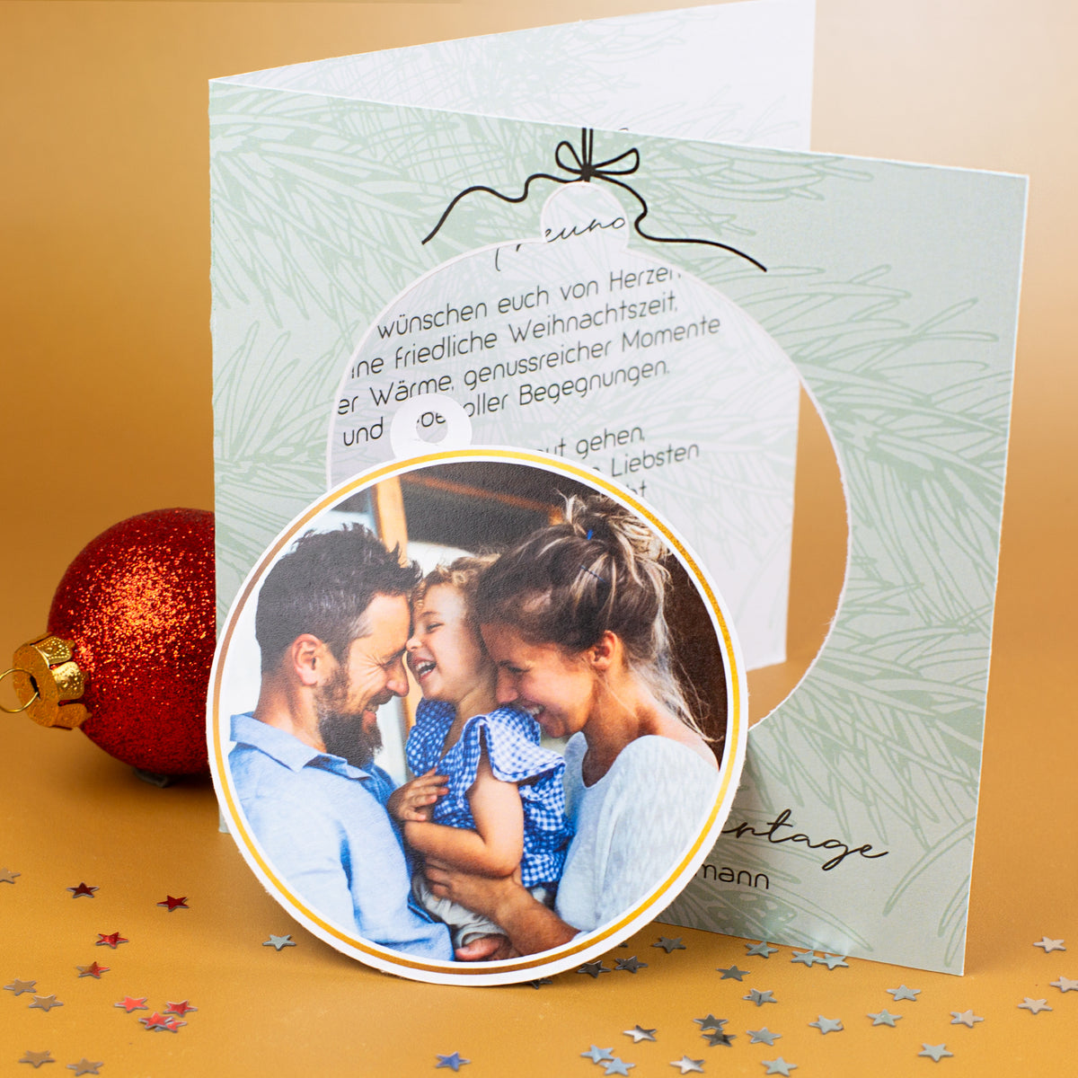 Geöffnete Weihnachtskarte mit kreisförmiger Aussparung links, herausgenommener Fotokugel im Vordergrund und gedrucktem Weihnachtsgrußtext auf der rechten Innenseite