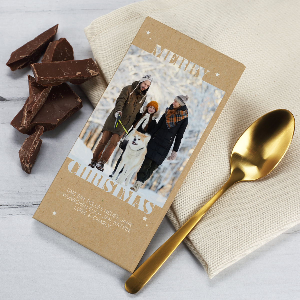 Weihnachtliche Schokolade mit personalisierter Verpackung und integriertem Foto. Die Tafel zeigt eine Familie beim winterlichen Spaziergang mit Hund, kombiniert mit dem festlichen Schriftzug „Merry Christmas“. Das Design wirkt edel und natürlich durch den Kraftpapier-Look und den dezenten Sternenaufdruck. Ideal als kleines Geschenk oder Wichtelidee für die Adventszeit.