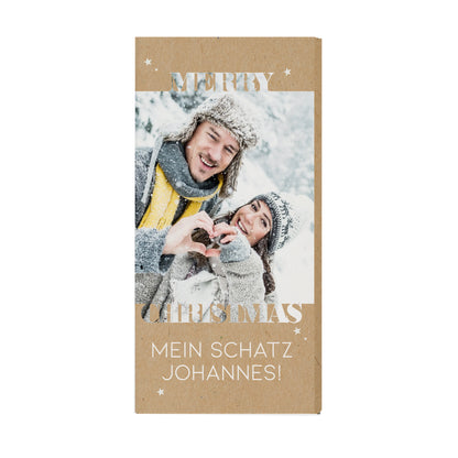 Personalisierte Weihnachts-Schokolade mit eigenem Foto und individuellem Text im modernen Naturdesign. Die Verpackung zeigt ein lachendes Paar im Schnee mit Herzmotiv aus den Händen, darüber steht „Merry Christmas“ in großen Lettern. Ein süßes, persönliches Präsent für Partner, Freunde oder Familie, gefüllt mit 100 g zarter Vollmilchschokolad