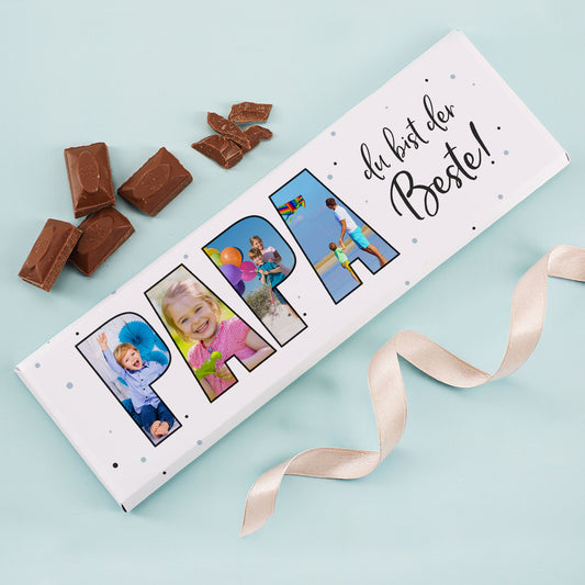 XXL Schokoladentafel „Papa du bist der Beste!“ mit 4 personalisierten Fotos und Milchschokolade-Stücken daneben auf hellblauem Hintergrund