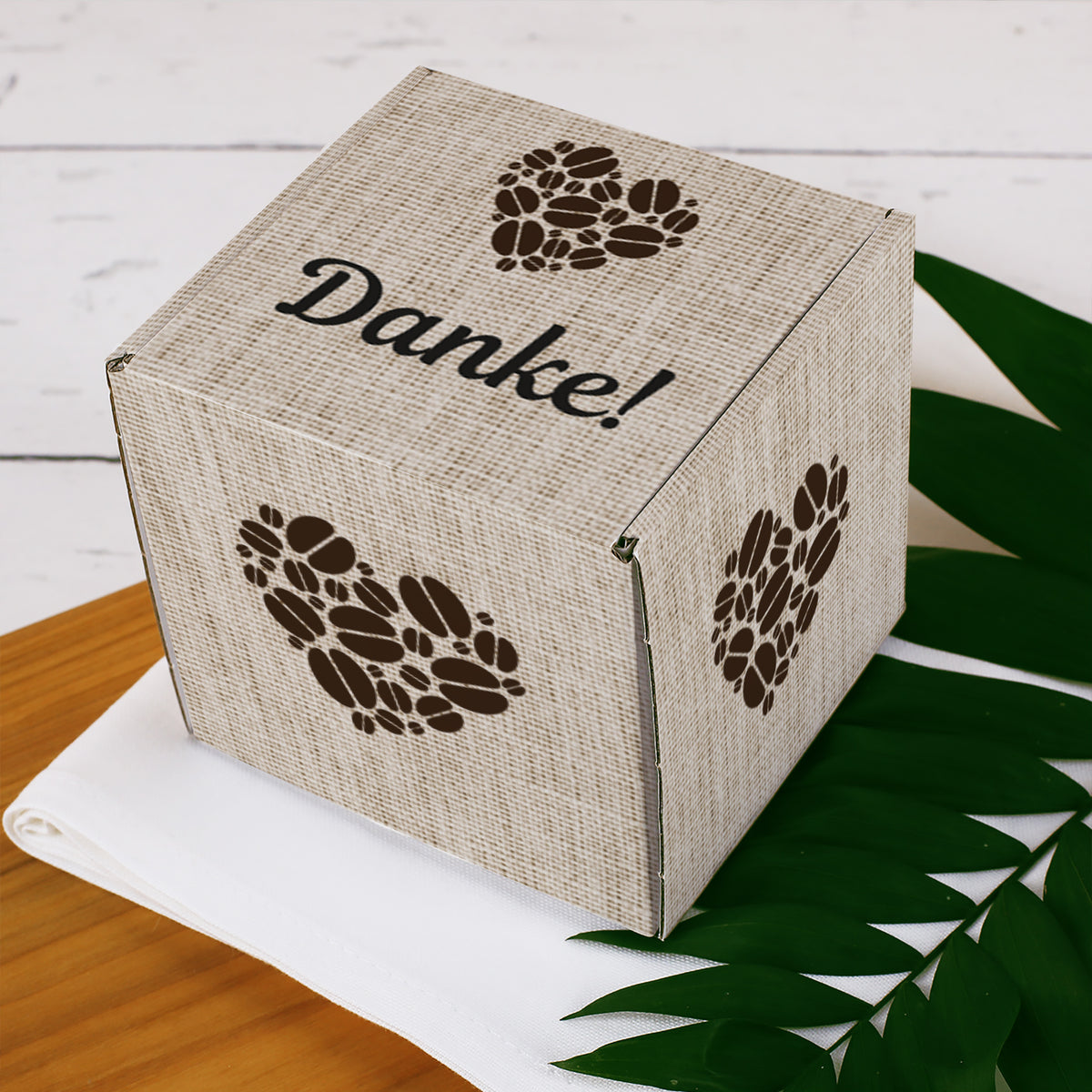 Geschenkbox für Kaffeetassen mit Herz aus Kaffeebohnen und personalisiertem Wunschtext auf dem Deckel, geschlossen dargestellt.