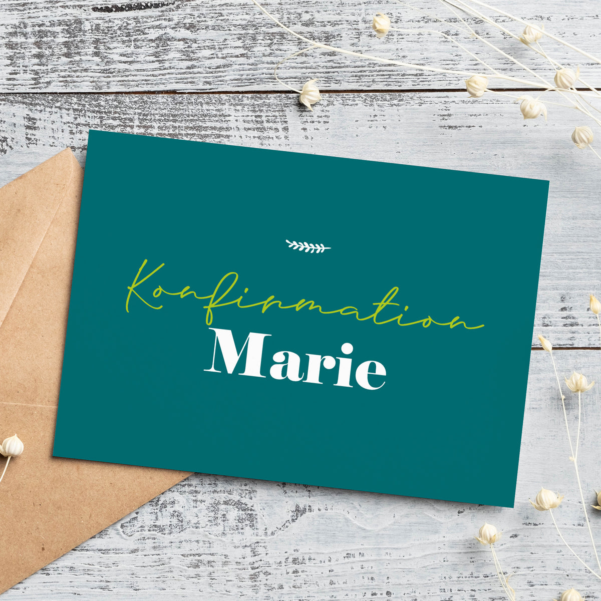 Personalisierte Einladungskarte zur Konfirmation in stilvollem Petrolgrün. Die Vorderseite trägt den Schriftzug „Konfirmation Marie“ in eleganter Schrift mit einer kleinen Ziergrafik darüber. Die Karte liegt auf einem weißen Holztisch mit einem braunen Briefumschlag und filigranen Trockenblumen, passend zur natürlichen Gestaltung.
