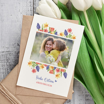 Osterkarte mit Foto und Blumenmotiv neben Umschlag und Tulpen dekorativ arrangiert