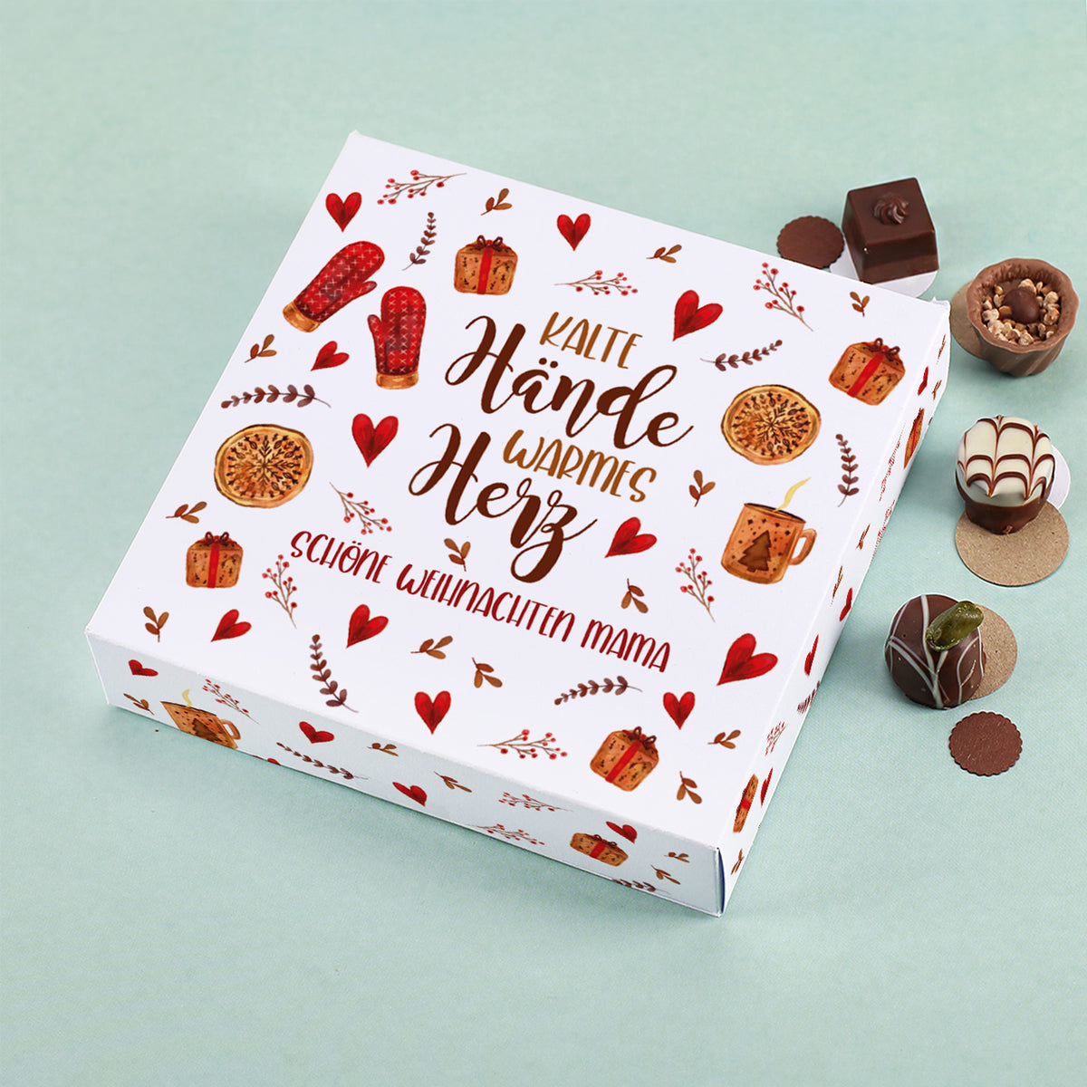 Lindt Pralinenbox mit Motiv „Kalte Hände, warmes Herz“ und personalisiertem Wunschtext „Schöne Weihnachten Mama“, umgeben von Schokolade und Pralinen auf mintgrünem Hintergrund.