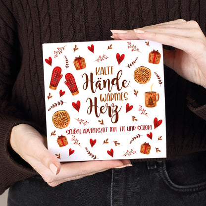 Personalisierte Lindt Pralinenverpackung mit Motiv „Kalte Hände, warmes Herz“ und Wunschtext „Schöne Adventszeit mit Tee und Schoki“, gehalten in zwei Händen vor dunklem Pullover.