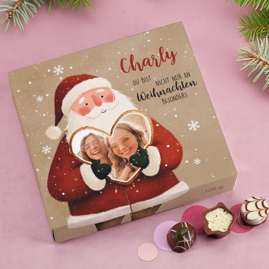 Der Weihnachtsmann in rotem Mantel hält ein Herz mit eingedrucktem Foto von zwei lachenden jungen Frauen. Darüber personalisierter Name „Charly“ und Wunschtext „Du bist nicht nur an Weihnachten besonders“.