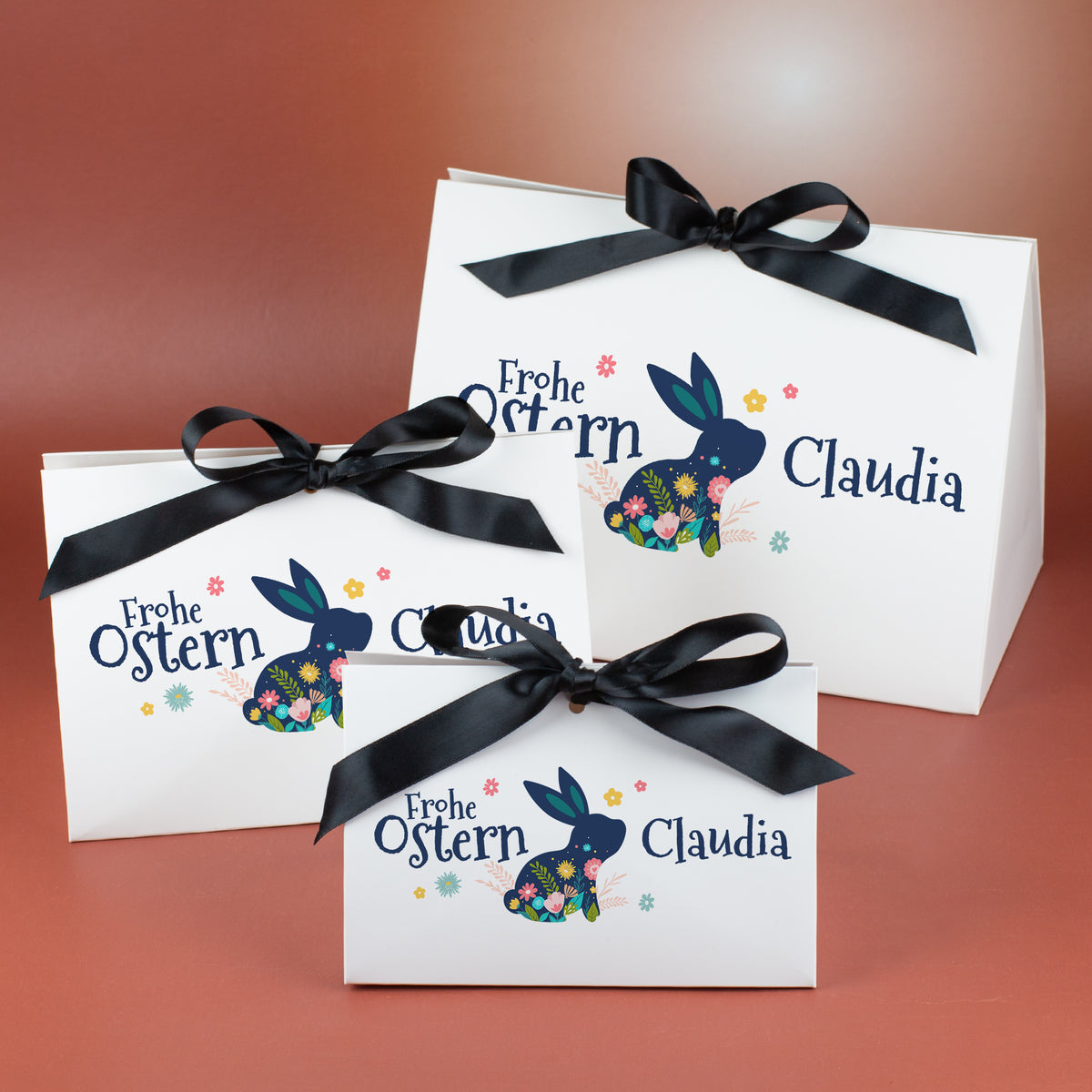 Drei personalisierte Oster-Geschenkverpackungen mit floralem Hasenmotiv und schwarzer Satinschleife