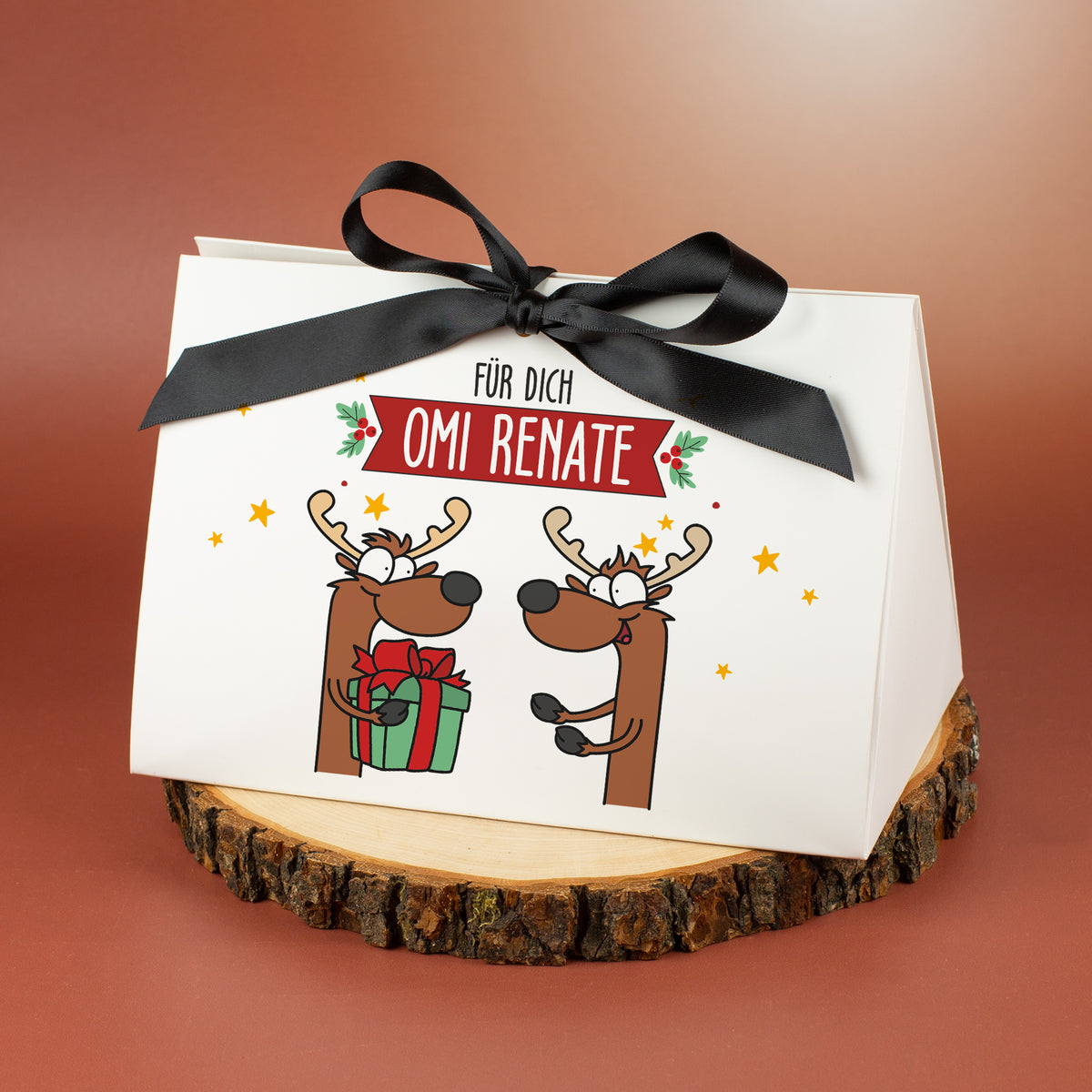 Geschenkverpackung mit Rentiermotiv und Name „Omi Renate“, mittlere Größe, auf Holzscheibe gezeigt.