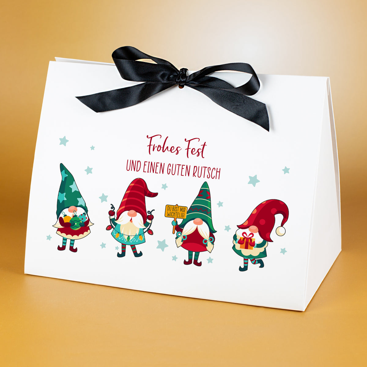 Weihnachtliche Geschenktasche in großer Größe, dekoriert mit schwarzer Satinschleife. Aufgedruckt ist ein farbiges Wichtelmotiv aus vier Figuren sowie der Weihnachtsgruß „Frohes Fest und einen guten Rutsch“. Die Tasche aus mattweißem Karton steht auf goldenem Hintergrund und zeigt das Motiv großformatig und detailgenau.