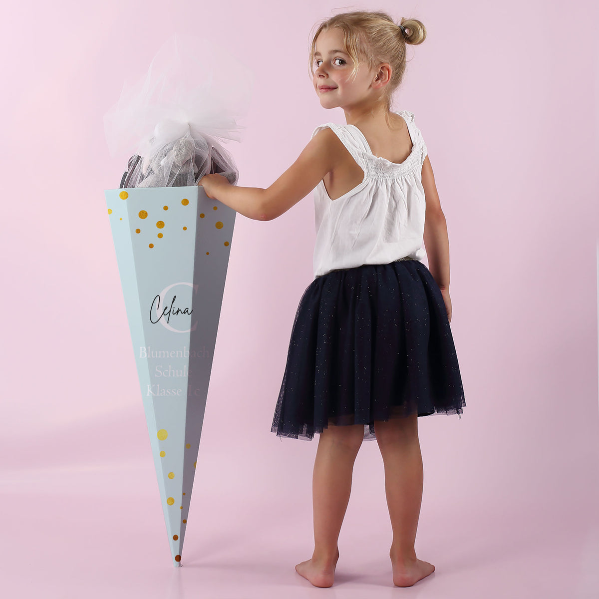 Mädchen von hinten mit hellblauer Schultüte, weißem Tüll und Namen auf der Rückseite