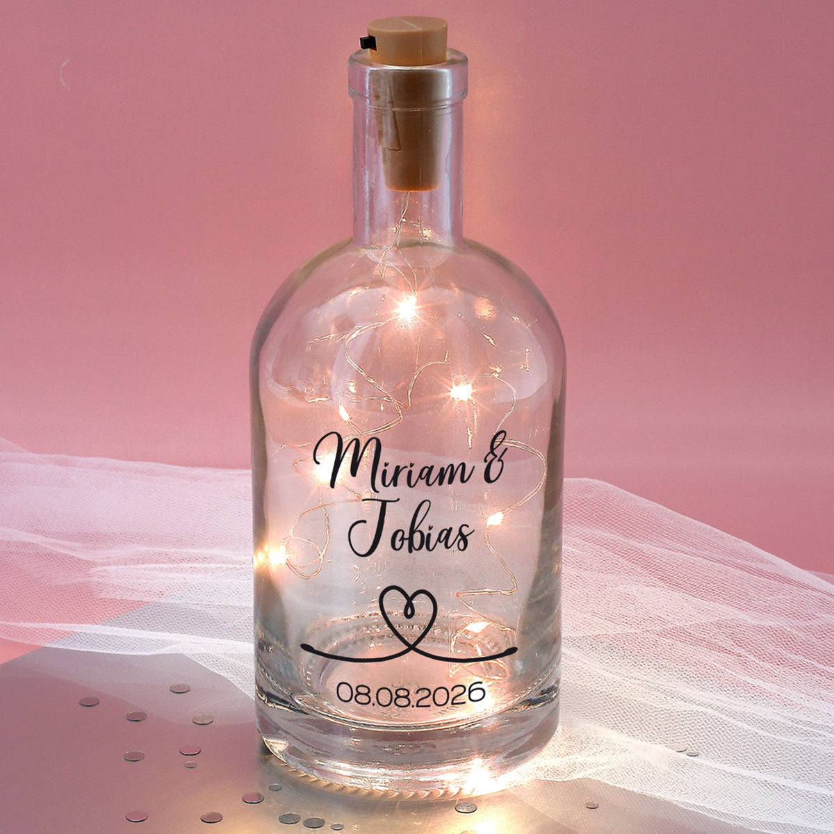 Bedruckte Glaskaraffe mit LED-Lichterkette vor rosa Hintergrund