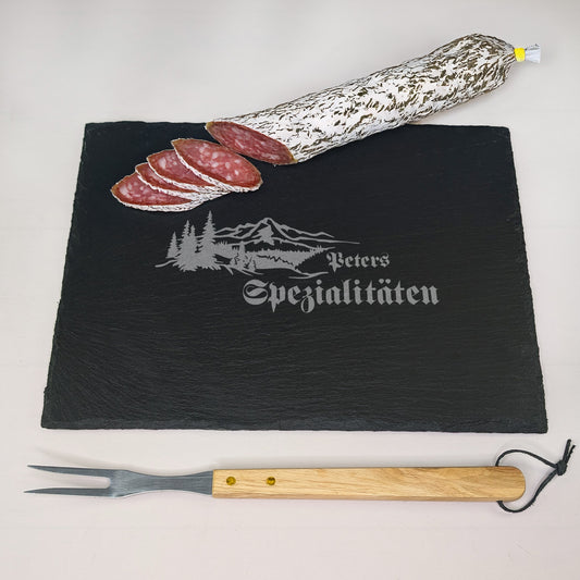 Rechteckige Schieferplatte mit Gravur „Peters Spezialitäten“ und Landschaftsmotiv, belegt mit Salami und Fleischgabel