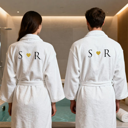 Zwei Personen im Spa-Bereich in weißen Bademänteln mit bestickten Initialen und Herz, Partnerlook von hinten