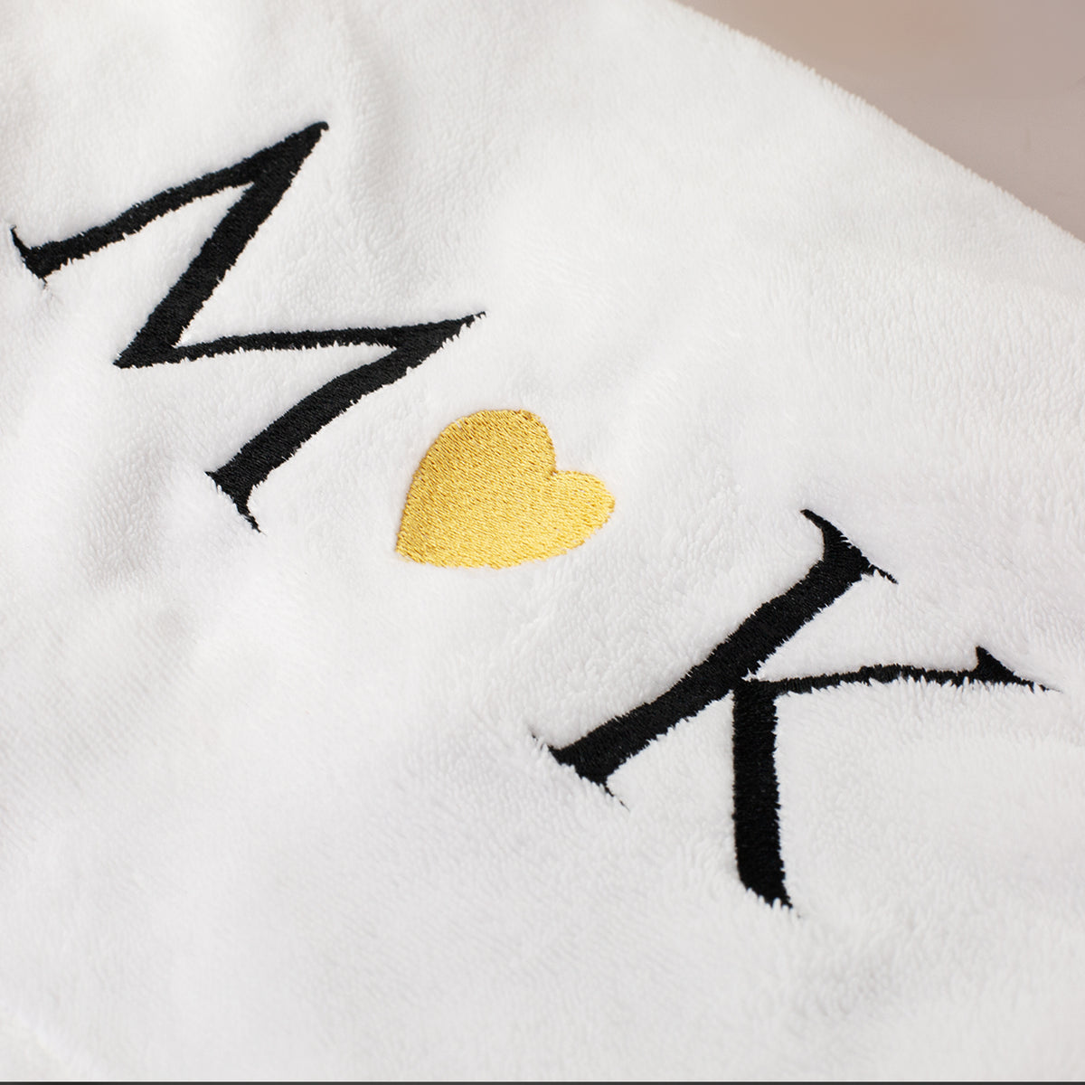 Detailaufnahme der Stickerei mit personalisierten Initialen und goldenem Herz auf weißem Handtuch