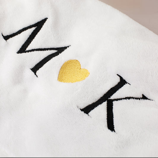 Detailaufnahme der Stickerei mit personalisierten Initialen und goldenem Herz auf weißem Handtuch