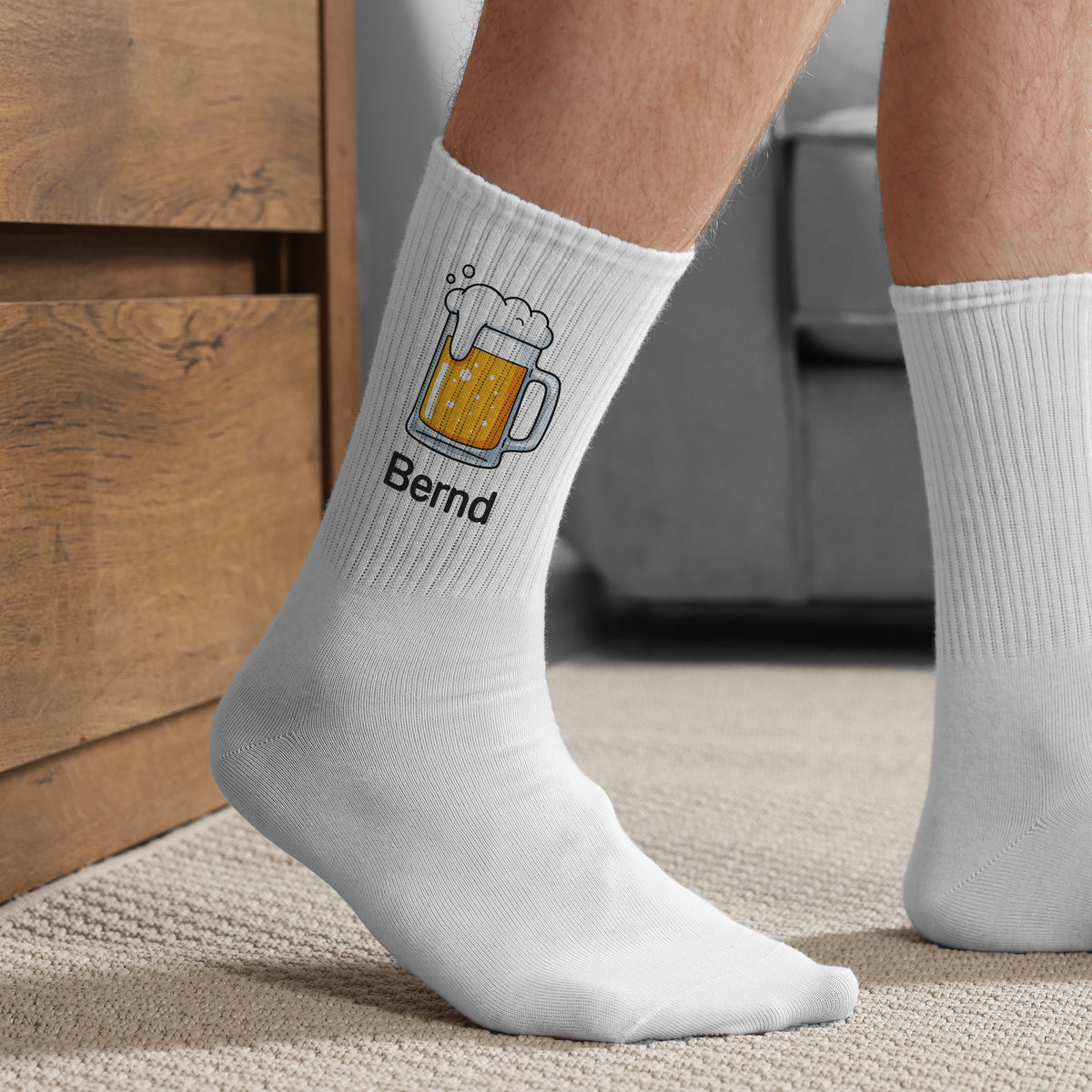 Getragene weiße Socken mit Bierkrug-Motiv und Name „Bernd“ – Detailansicht seitlich auf Teppichboden.