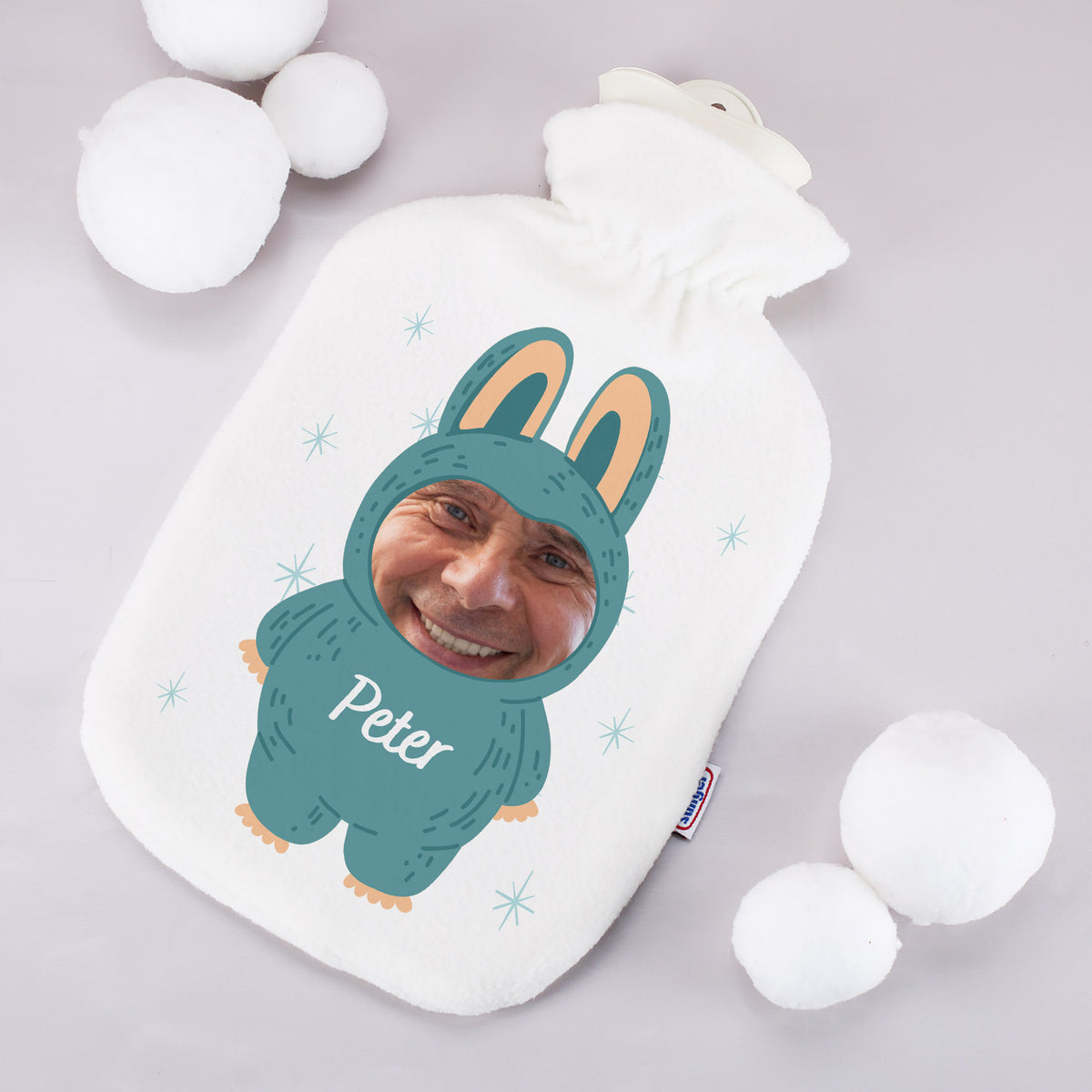 Wärmflasche mit Monster-Design, Foto und Name „Peter“ bedruckt, liegend zwischen Deko-Schneebällen
