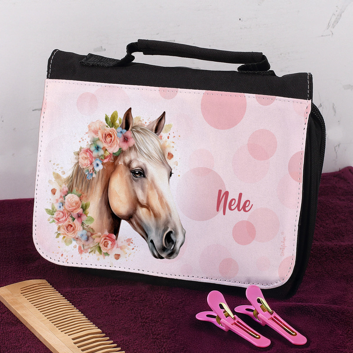 Schwarze Waschtasche mit rosa Pferdemotiv und Name „Nele“ auf Handtuch mit Kamm und Haarclips