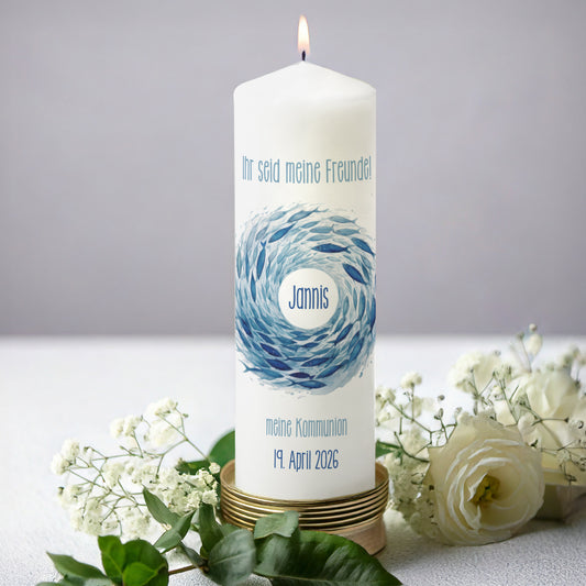 Blaue Fischschwarm-Kerze zur Kommunion mit Wunschtext – Eine weiße Kerze mit einem dynamischen Fischschwarm-Motiv in tiefen Blautönen. Der Name ist mittig eingefügt, mit einem personalisierbaren Spruch wie „Ihr seid meine Freunde!“ darüber. Der Anlass „Meine Kommunion“ und das Datum sind darunter aufgedruckt. Die Kerze steht auf einer goldenen Halterung, umgeben von weißen Blüten.