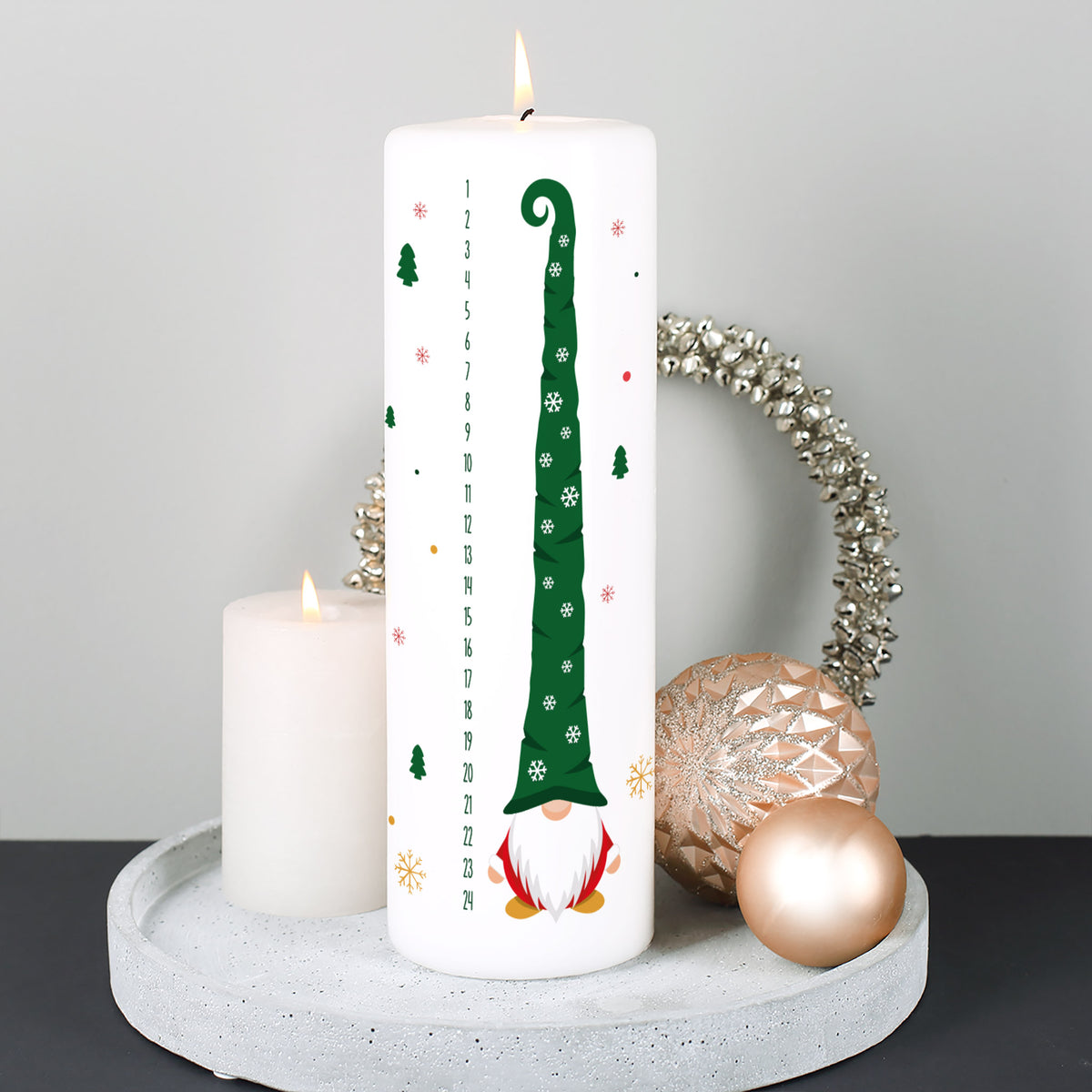 Adventskerze mit Wichtelmotiv brennend auf Dekotablett mit Weihnachtskugeln