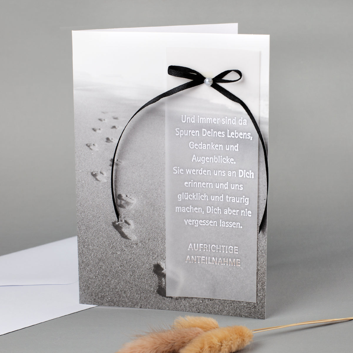 Trauerkarte mit Motiv Spuren im Sand und silbergeprägtem Text sowie schwarzer Schleife